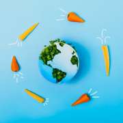 Creative veganism concept with rockets of carrots and baby corn flying around planet Earth, Earth model made of paper and fresh green sprouts collage on blue background.