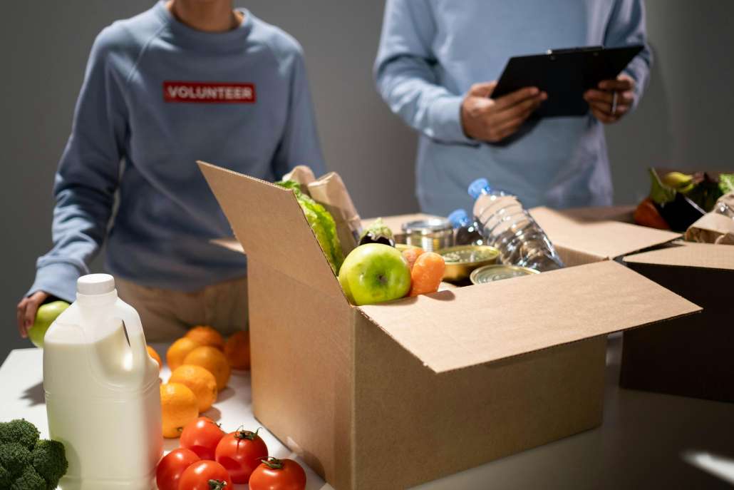 Two volunteers packing food and drinks inside cardboard boxes.